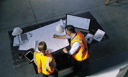 Un homme et une femme se tiennent près d'une table et examinent des plans de construction